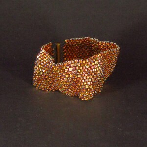 May include: A gold-toned bracelet made of small, iridescent beads woven into a wavy pattern.