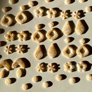 May include: Assortment of small, decorative, beige and gold-flecked resin shapes, including flowers, stars, and geometric shapes.