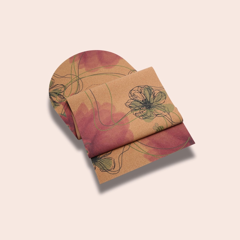 May include: A cork yoga mat with a floral design in shades of brown, pink, and green. The mat is rolled up and the design is visible on the outside of the roll.