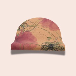 May include: A rolled up cork yoga mat with a floral design featuring pink and green flowers and a bee. The mat has a light brown background.