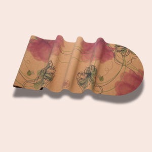 May include: A rolled up cork yoga mat with a floral design featuring pink watercolour flowers and green leaves. The mat has a brown cork background with a subtle texture.