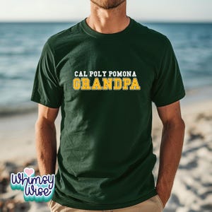 May include: Dark green t-shirt with the text "CAL POLY POMONA GRANDPA" in white and gold lettering. The shirt is a crew neck and short-sleeved. The background shows a beach scene.