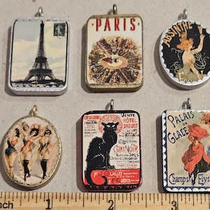 May include: A set of ten vintage-style metal charms featuring various images. The charms are silver, gold, and blue with images of a black cat, a Parisian scene, a woman in a dress, and a woman in a hat. The charms are perfect for adding a touch of vintage style to your jewelry or crafts.