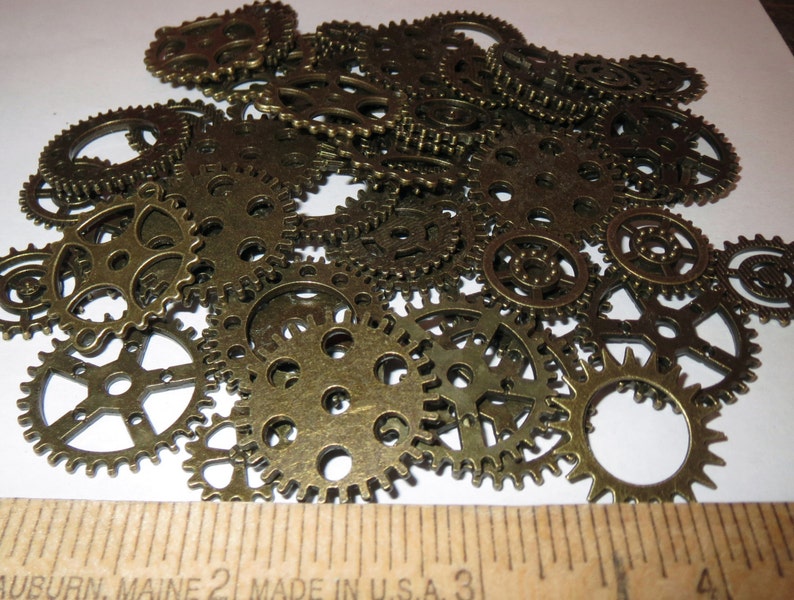 May include: A pile of antique gold-toned metal gears of various sizes. The gears are arranged in a random pattern and are all in focus.