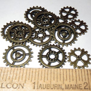 May include: A collection of ten bronze-colored metal gears of various sizes. The gears have a detailed design with small teeth around the edges.