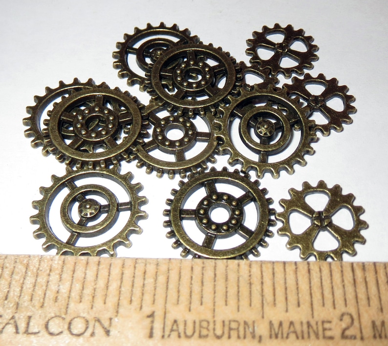 May include: A collection of ten bronze-colored metal gears of various sizes. The gears have a detailed design with small teeth around the edges.