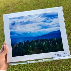 Puede incluir: Una fotografía enmarcada de una cordillera con un cielo azul y nubes blancas. Las montañas están cubiertas de árboles y el cielo es de un azul claro. La foto está enmarcada en un marco blanco y tiene una etiqueta que dice "Great Smoky Mountains, TN -  High up elevation - ZSS Photography @zssphoto".
