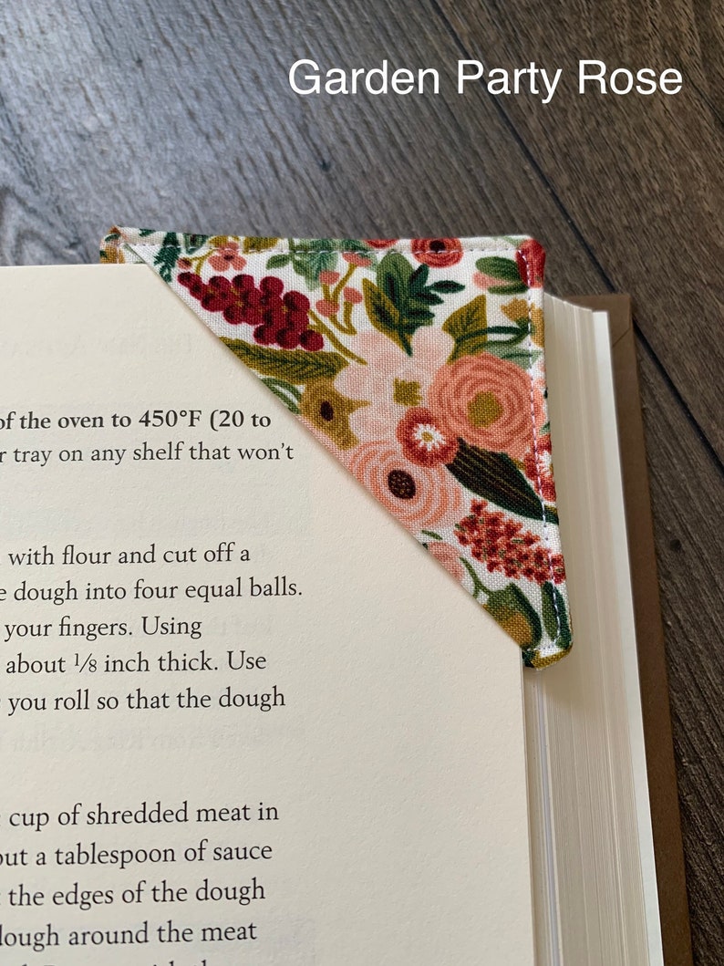 May include: A triangular bookmark with a floral pattern in shades of pink, red, and green. The bookmark is made of fabric and has a stitched edge. The text "Garden Party Rose" is visible at the top of the image.