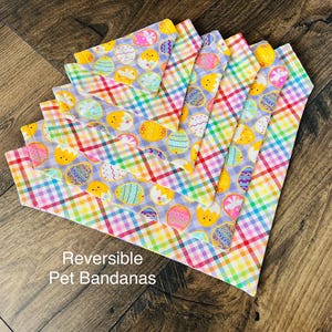 May include: A set of six reversible pet bandanas featuring a colorful plaid pattern with a pastel purple background and a repeating pattern of yellow Easter eggs. The text "Reversible Pet Bandanas" is printed on the bottom of the image.