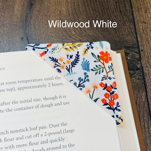 May include: A white fabric bookmark with a floral pattern in shades of blue, orange, and yellow. The bookmark is folded into a triangle shape and has the text "Wildwood White" printed on the top.