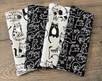 May include: Four fabric cases with cat patterns. The cases feature black and white cat illustrations on a light gray and black background. Each case has a snap closure. The cases are arranged on a wooden surface.