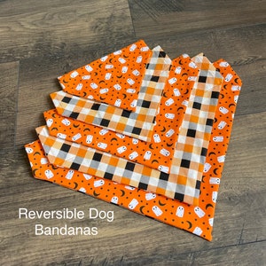 May include: Five reversible dog bandanas in orange and white with a ghost and crescent moon pattern on one side and a black and white checkered pattern on the other side. The text "Reversible Dog Bandanas" is printed below the bandanas.