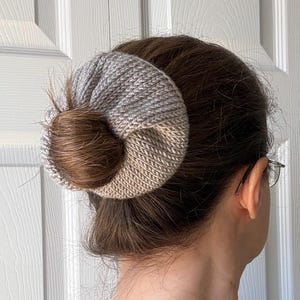 May include: A knitted hair bun cover in shades of gray and beige. The hair accessory is wrapped around a bun, creating a stylish and functional hair updo. The knitted texture adds a touch of handmade charm to the hairstyle.