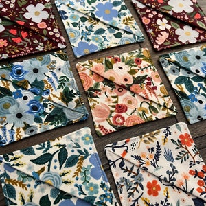 May include: A set of 10 square fabric coasters with a variety of floral patterns in shades of blue, red, and white. The coasters are made of cotton fabric and have a stitched edge.
