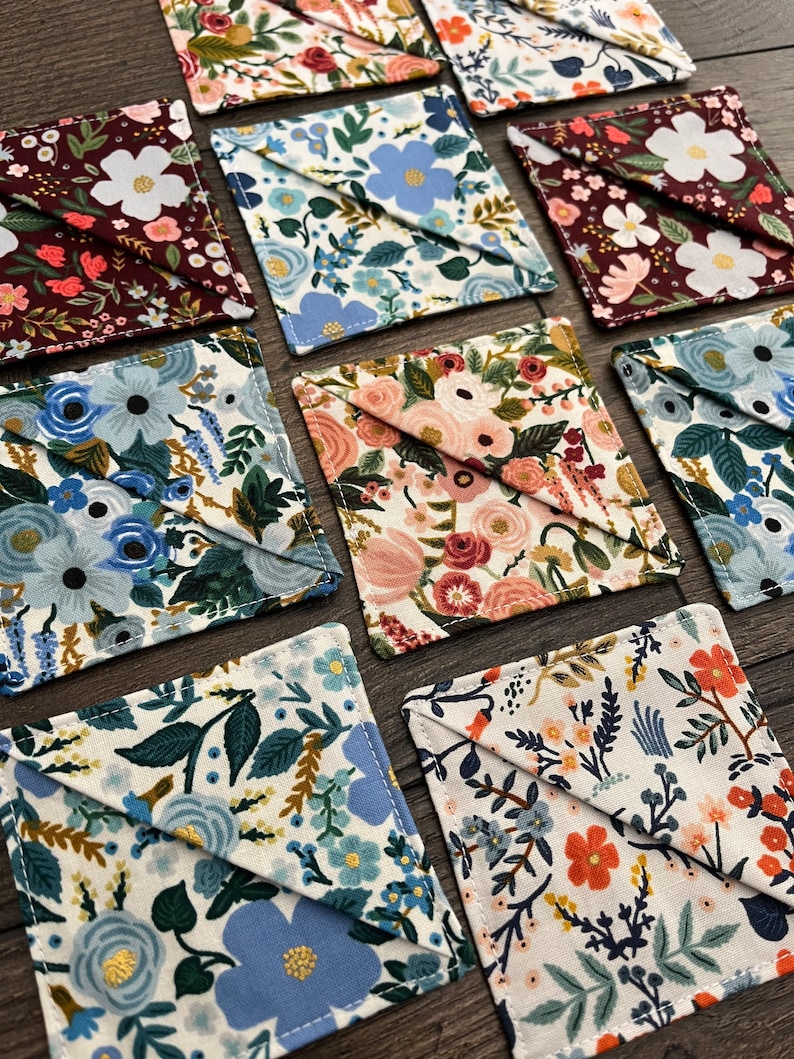 May include: A set of 10 square fabric coasters with a variety of floral patterns in shades of blue, red, and white. The coasters are made of cotton fabric and have a stitched edge.