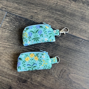 May include: Two small, matching coin purses with a floral pattern in shades of blue, yellow, and white on a light blue background. Each purse has a zipper closure and a small loop or clip for attachment.
