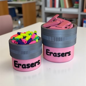 May include: Two pink eraser holders with gray tops, labeled "Erasers" in black. One is filled with colorful pencil-shaped erasers, the other with rectangular pink erasers. The holders sit on a white surface.