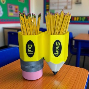 May include: A yellow pencil-shaped desk organizer with two compartments, one labeled "Dull" and the other "Sharp." Each compartment holds several yellow pencils with pink erasers. The organizer sits on a wooden desk in a classroom setting.