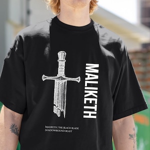 May include: Black t-shirt featuring a white illustration of a sword with the text "MALIKETH" vertically on the right side. Below the sword is the text "MALIKETH, THE BLACK BLADE SHADOWBOUND BEAST".
