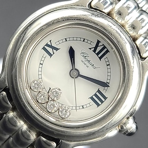 May include: A silver-toned Chopard watch with a white face, featuring black Roman numerals and hands. The watch face includes the brand name and five diamond accents. The watch has a silver band.