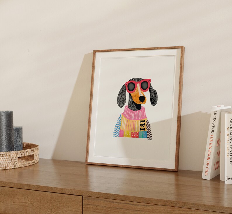 K&ouml;nnte beinhalten: Eine gerahmte Illustration eines schwarz-wei&szlig;en Hundes, der eine rosa Sonnenbrille und einen bunten Pullover tr&auml;gt. Der Hund schaut direkt auf den Betrachter.