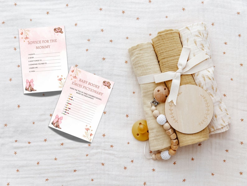 Peut inclure: Deux cartes de jeu de baby shower roses et blanches avec des motifs floraux. La premi&egrave;re carte dit "Conseils pour la maman" et contient une liste d'invites. La deuxi&egrave;me carte dit "Pictionary des livres pour b&eacute;b&eacute;s Emoji" et contient une liste d'emojis. Un hochet pour b&eacute;b&eacute; en bois, un cercle en bois avec un motif floral et un ensemble de trois langes en mousseline beige attach&eacute;s avec un ruban blanc sont sur un fond blanc avec de petites &eacute;toiles brunes.