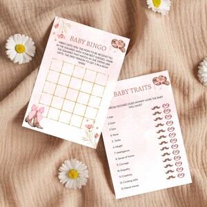 Peut inclure: Deux cartes de jeu de baby shower roses et dor&eacute;es. La premi&egrave;re carte est une carte de bingo avec le titre "Baby Bingo". La deuxi&egrave;me carte est un jeu de traits de b&eacute;b&eacute; avec le titre "Baby Traits".