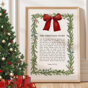 May include: A framed print featuring "The Christmas Story" text and a red bow design, framed by a green garland with red berries. A Christmas tree with decorations and presents is visible in the background.