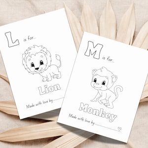 May include: Two white cards with black line drawings of a lion and a monkey, with the words "Lion" and "Monkey" below. The cards also have the text "L is for..." and "M is for..." above the drawings. The cards are on a beige surface.