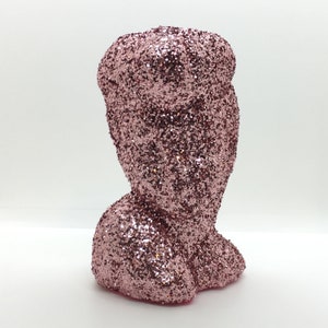 May include: A pink glitter vase with a unique shape. The vase is made of ceramic and has a smooth, shiny finish.