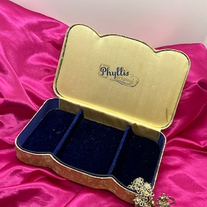 May include: A vintage jewelry box with a gold and blue velvet interior. The box has a raised, scalloped edge and is labeled "Phyllis Original" on the lid.
