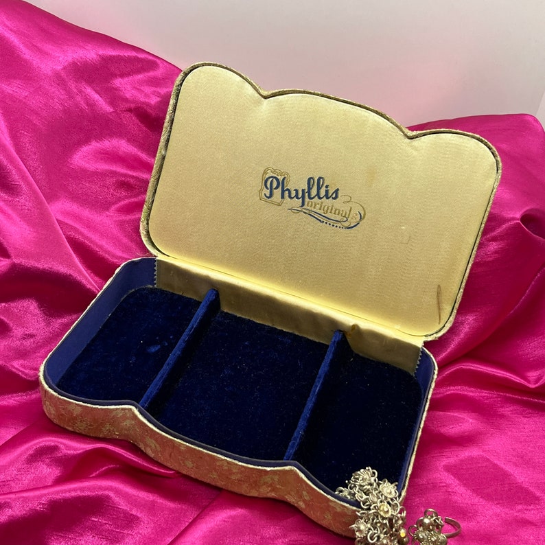 May include: A vintage jewelry box with a gold and blue velvet interior. The box has a raised, scalloped edge and is labeled "Phyllis Original" on the lid.