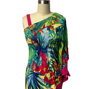 May include: A one-shoulder top featuring a vibrant tropical print with green palm leaves, bright red hibiscus flowers, and yellow accents. The garment includes a solid hot pink strap and a matching hot pink hemline with a gathered, elasticized waist.