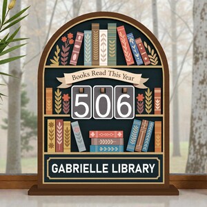 May include: A wooden bookshelf-shaped sign with the text "Books Read This Year" and "506". The sign has a dark blue background with colorful book illustrations and the text "GABRIELLE LIBRARY".