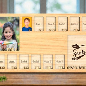 Può includere: Una cornice in legno per gli anni scolastici, dalla scuola materna all'ultimo anno. La cornice ha spazi per le foto e la scritta "Senior 2026 GRADUATION". Include spazi per ogni livello scolastico.