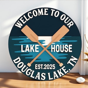 May include: A round wooden sign with the words "WELCOME TO OUR LAKE HOUSE DOUGLAS LAKE, TN" in white lettering. The sign features crossed oars and a lake scene in blue and white. The year "EST.2025" is also displayed.