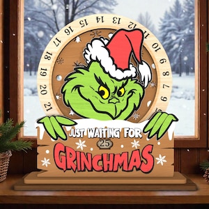 May include: Wooden Christmas countdown calendar featuring the Grinch with a red Santa hat. The calendar has a circular design with numbers and the text "JUST WAITING FOR GRINCHMAS". The Grinch is green with a grumpy expression.