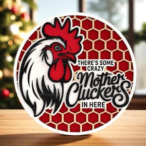 Può includere: Un cartello rotondo in legno con un disegno di gallo. Il cartello ha uno sfondo rosso a nido d'ape e il testo "THERE'S SOME CRAZY Mother Cluckers IN HERE". Il gallo ha cresta e bargigli rossi.