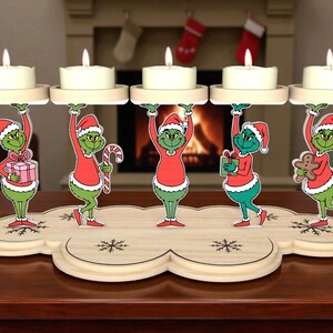 Puede incluir: Un portavelas navideño de madera con cinco figuras del Grinch sosteniendo plataformas para velas. Cada figura del Grinch viste un traje y gorro de Papá Noel rojos, con cara y vientre verdes. La base es de madera clara con recortes de copos de nieve.