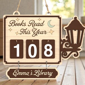 May include: Wooden sign with the text "Books Read This Year" and the number "108" displayed on brown number cards. The sign also includes the text "Emma's Library" and a decorative lantern.