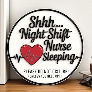 May include: Round wooden sign with the text "Shhh... Night Shift Nurse Sleeping" in black script. A red heart with a heartbeat line is in the center. The sign also includes the text "PLEASE DO NOT DISTURB! (UNLESS YOU NEED CPR)".