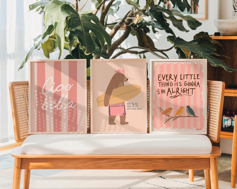 Pu&ograve; includere: Tre stampe artistiche incorniciate con sfondo a righe rosa chiaro e bianche. Una stampa dice "Ciao Bella", un'altra presenta un orso con una tavola da surf e la terza dice "Every Little Thing Is Gonna Be Alright" con uccelli.