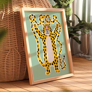 K&ouml;nnte beinhalten: Eine gerahmte Illustration eines gelben und schwarzen Leoparden mit einem gefleckten Schwanz. Der Leopard h&auml;lt seinen Schwanz in die Luft und der Schwanz bildet das Wort "Roar". Der Hintergrund ist hellblaugr&uuml;n.