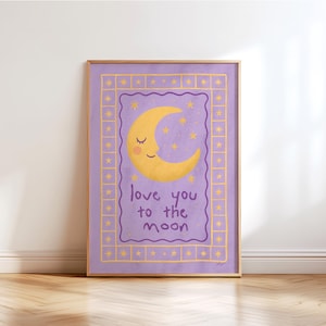 Puede incluir: Una impresión artística enmarcada con una luna creciente amarilla y estrellas sobre un fondo morado. El texto "love you to the moon" está escrito en púrpura. El marco es dorado. La impresión está sobre un suelo de madera.