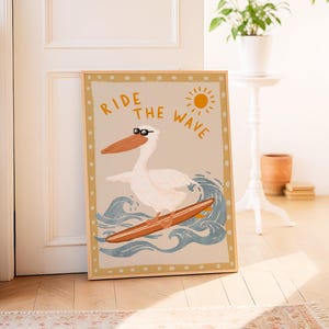 K&ouml;nnte beinhalten: Ein beige-brauner gerahmter Druck mit einem wei&szlig;en Pelikan, der eine Sonnenbrille tr&auml;gt und auf einer blauen Welle surft. Der Text "Ride the Wave" ist in gelben und orangefarbenen Buchstaben geschrieben.