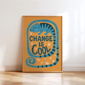 Puede incluir: Un póster enmarcado con un diseño de camaleón azul y el texto "CHANGE IS COOL". El póster tiene un fondo naranja cálido y está en un marco de madera. La cola del camaleón rodea el texto.