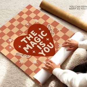 May include: A poster featuring a red heart design with the words "THE MAGIC IS YOU" on a peach and white checkered pattern. The poster is being unrolled, with the text "YOU CAN PRINT AS MANY AS YOU LIKE" visible.