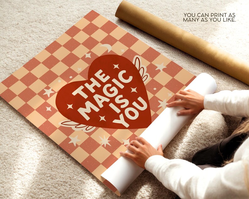 May include: A poster featuring a red heart design with the words "THE MAGIC IS YOU" on a peach and white checkered pattern. The poster is being unrolled, with the text "YOU CAN PRINT AS MANY AS YOU LIKE" visible.