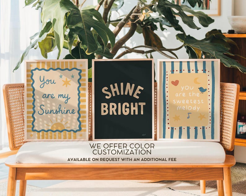May include: Three rectangular wall art prints in light wood frames. The left print features yellow stripes, a blue scalloped border, and the text "You are my Sunshine". The center print is black with the text "SHINE BRIGHT". The right print has blue stripes and the text "you are the sweetest melody".