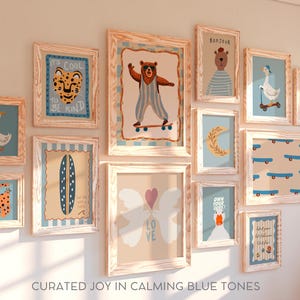 May include: A gallery wall of framed prints with a blue and white color scheme. The prints feature various designs, including animals, words, and abstract patterns. The frames are all made of light wood and have a rustic look. The text on the prints includes "It's Cool to Be Kind", "Bonjour", "Own Your Sparkle", and "Love".